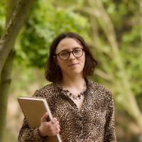 A photograph of Holly holding a sketchbook with trees in the background 