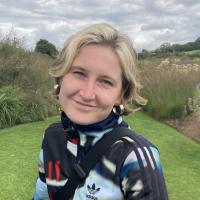 Person with short blonde hair, in a garden, smiling at the camera